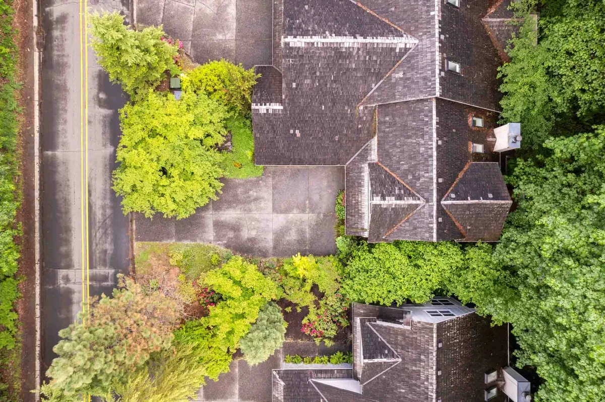 An exterior view filled with lush greenery, showcasing rooflines and a driveway, with a serene mood. The space is perfect for outdoor relaxation, possibly where guests could enjoy morning coffee or unwind after a round of golf. The trees and patio area connect to the idea of alfresco dining and natural beauty.
