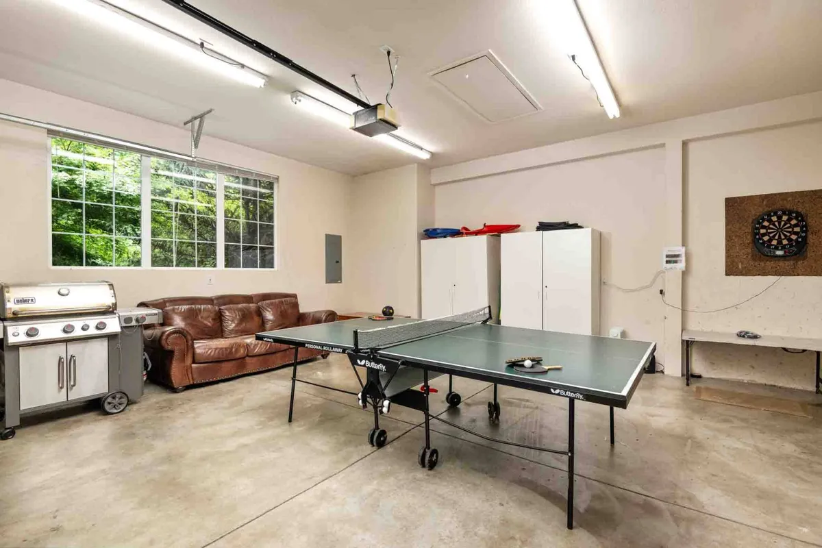 A spacious and inviting game room featuring a ping pong table, leather couch, grill, and dartboard. The playful atmosphere hints at friendly family competitions, relaxation, and shared laughter after a day of outdoor fun.