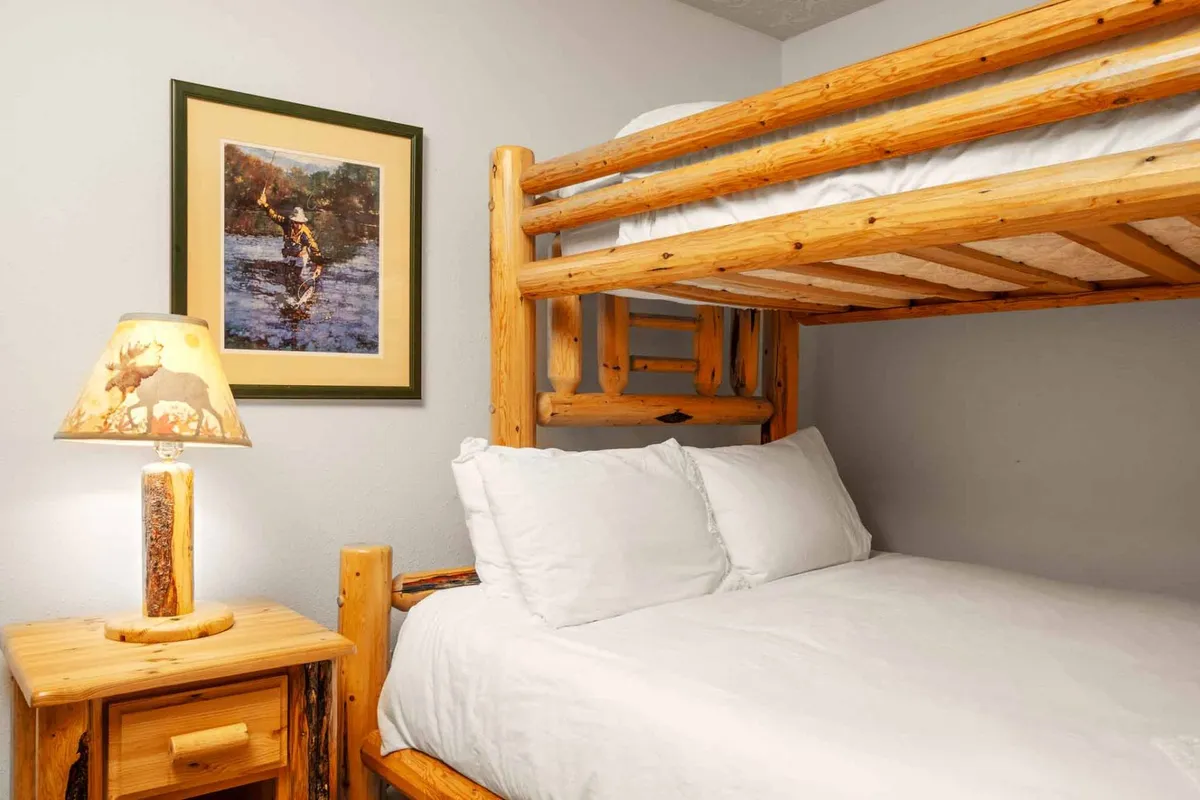 A cheerful bunk room with a twin-over-full bunk bed, nightstand with a lamp, and framed artwork on the wall. The space is designed for both rest and playful sleepovers, appealing to families and groups.
