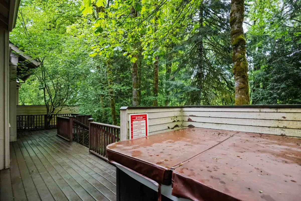 This exterior shot captures a spacious wooden deck nestled among tall pines, featuring a private hot tub and seating area. The tranquil atmosphere is enhanced by the surrounding forest and the sense of seclusion, with glimpses of nature and the golf course beyond.
