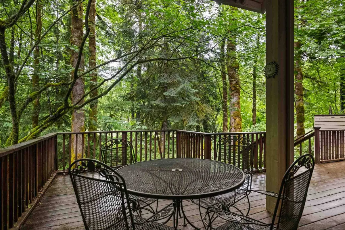 An inviting view of a deck with a metal outdoor dining table overlooking lush trees. The wooden railing and natural surroundings make this an ideal spot for alfresco meals, wildlife watching, or simply enjoying peaceful moments outdoors.
