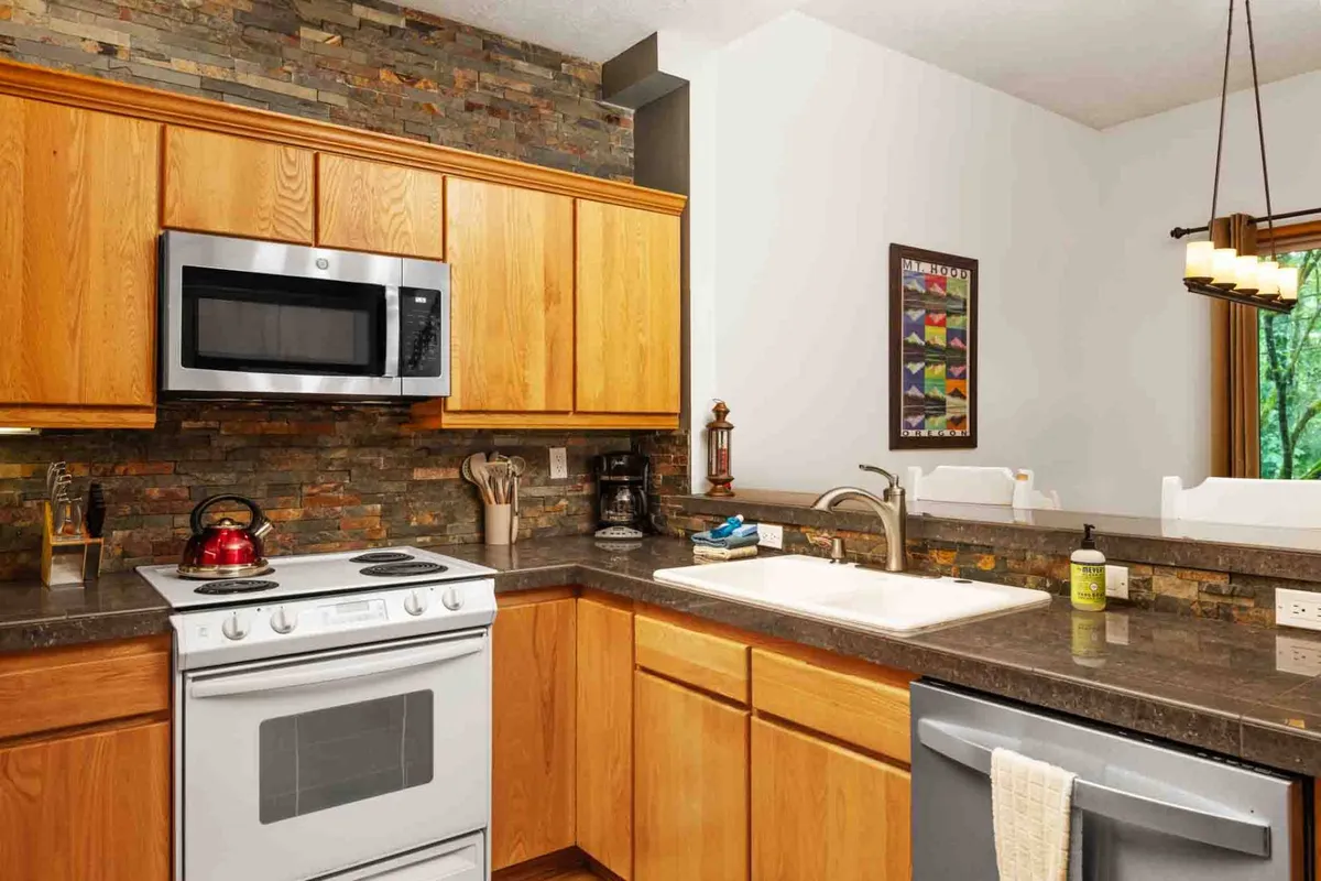 This image highlights a welcoming kitchen space featuring a prominent kitchen island, a stunning custom stone backsplash, stainless steel appliances, and a window that invites natural light. The granite countertops are visible, and the layout suggests ample space for both cooking and gathering.