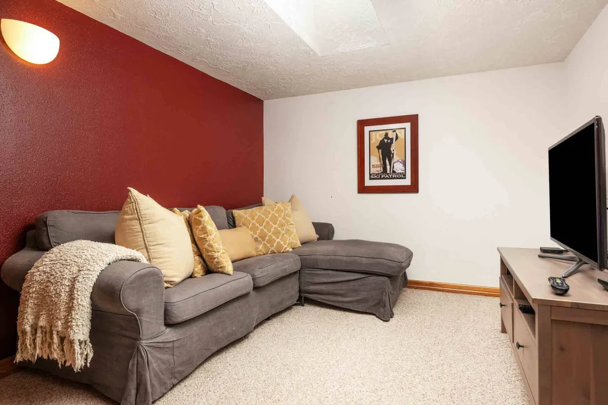 A welcoming living room featuring a spacious gray sectional couch adorned with decorative pillows. Framed artwork hangs on the wall, and a television is visible, suggesting a space perfect for group entertainment and relaxation.