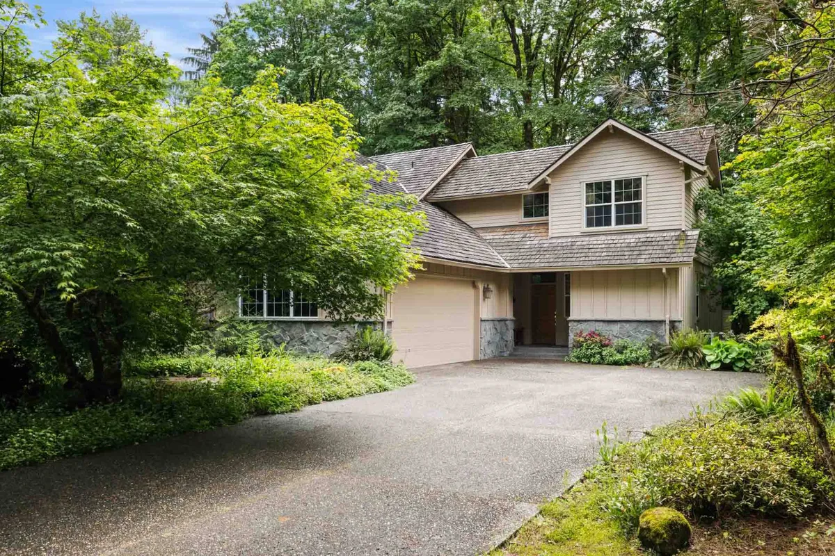 An exterior view of the home's front entrance surrounded by lush greenery and distinctive rooflines. The porch suggests a welcoming space for gathering, with the surrounding trees showcasing the tranquil, natural setting.