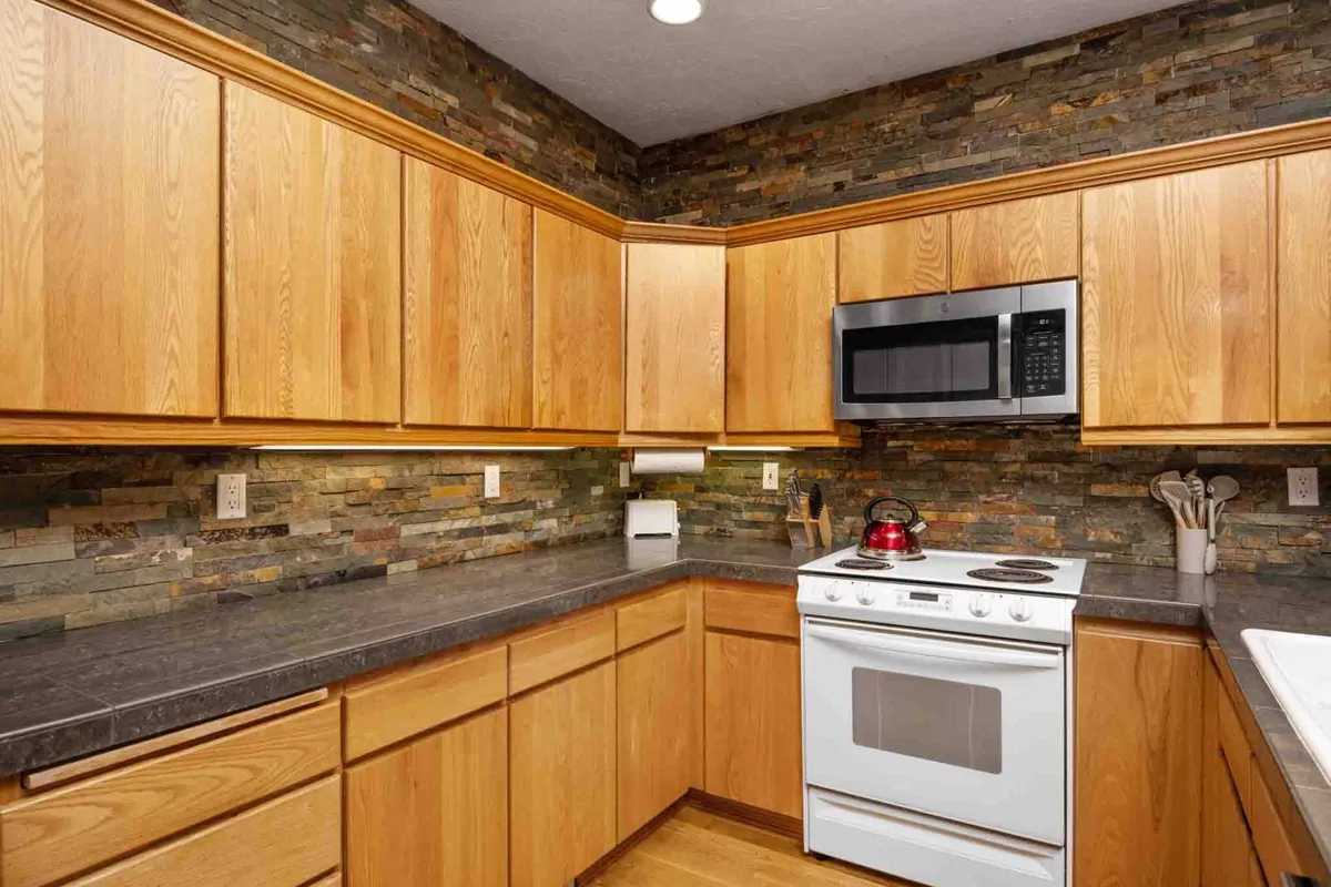 A warm, welcoming kitchen with wooden cabinets, a stone backsplash, and a white stove, inviting group meal preparation and shared dinners. The open layout offers space for social cooking and dining after an exciting day outside.